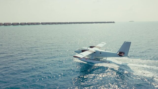 A magnificent seaplane gracefully taxis on the pristine turquoise water, approaching a luxurious tropical island resort lined with stunning overwater bungalows.
