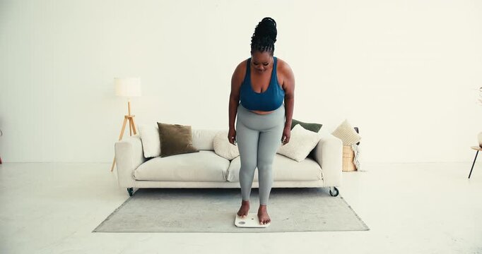 Overweight black woman in sportswear uses smart scale near sofa