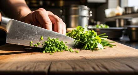 Fresh herbs being finely chopped on wooden cutting board in warm kitchen sunlight with stainless steel knife, closeup culinary preparation scene