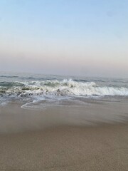 Ocean waves crashing on a sandy beach at sunset with a pastel sky