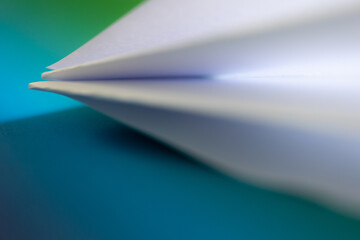 White paper airplane flying over a colorful background, representing concepts such as freedom,...
