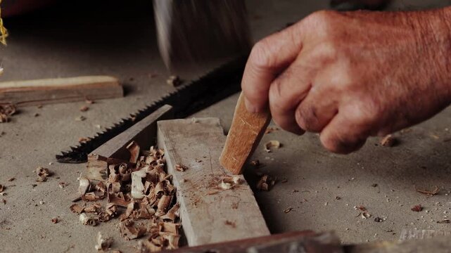 Close-up of a carpenter's hands using a hammer and a chisel to carve a piece of wood in a workshop. Video with original sound.