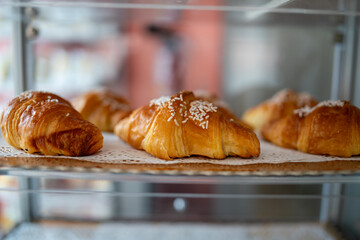 Freshly baked golden brown croissants sprinkled with sugar and arranged on a doily covered tray in...