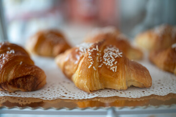 Freshly baked golden brown croissants sprinkled with sugar and arranged on a doily covered tray in...