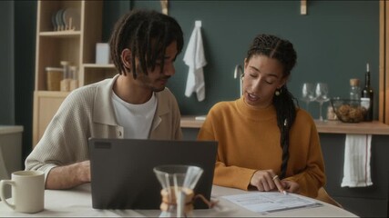 Medium shot of young biracial wife asking his husband about monthly expenses looking at domestic bills while calculating family budget together sitting at kitchen table at home - Powered by Adobe