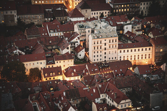 Aerial view of a tightly packed cityscape glows with warm light against the deepening dusk, showcasing the red-tiled roofs, Zagreb Cathedral, and historic buildings, Zagreb, Zagreb, Croatia.