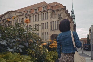 Woman exploring G&ouml;rlitz, Germany, with blooming flowers and historic architecture in the background. Travel, lifestyle, and European cityscape.