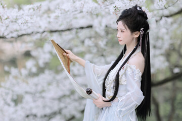 Elegant woman in traditional dress standing among cherry blossoms.