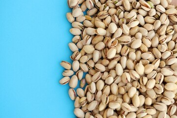 Tasty unpeeled pistachios on bright blue background, top view flat lay background pattern