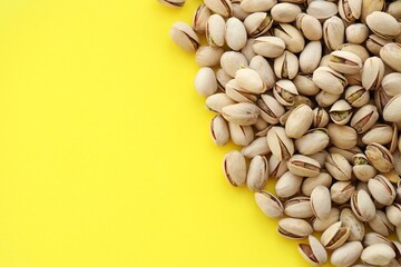 Tasty unpeeled pistachios on bright yellow background, top view flat lay background pattern