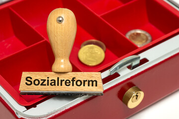 Ein Holzstempel ist beschriftet mit Sozialreform über einer leeren Kasse als Symbolbild für...