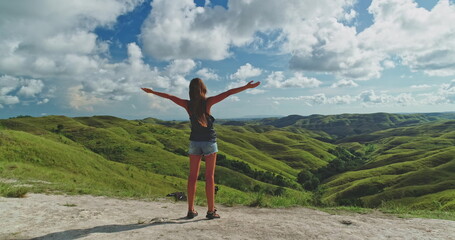 Young woman standing on a cliff with arms outstretched, embracing the breathtaking landscape of...