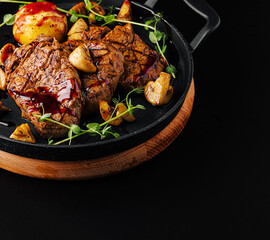 Juicy grilled steak with roasted potatoes and herbs on a black background