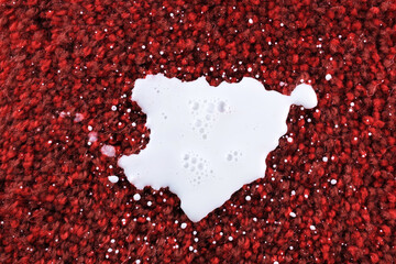 A white liquid milk contrasts vividly against a deep red textured surface.The bubbles and irregular...