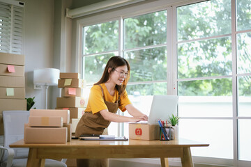 A young Asian female entrepreneur works from home, managing online sales, shipping parcels, marketing products, and ensuring client satisfaction efficiently.