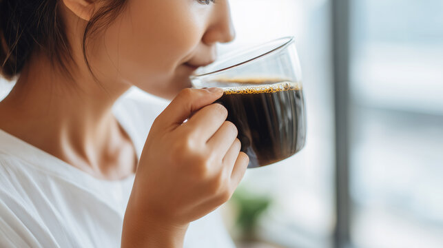 Woman enjoying a cup of hot black coffee in a clear glass mug during a relaxing morning.
