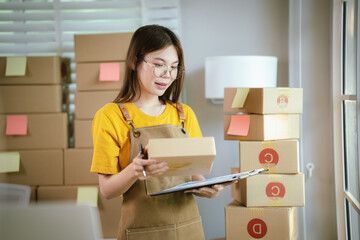 A young Asian female entrepreneur works from home, managing online sales, shipping parcels, marketing products, and ensuring client satisfaction efficiently.