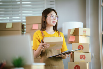 A young Asian female entrepreneur works from home, managing online sales, shipping parcels, marketing products, and ensuring client satisfaction efficiently.
