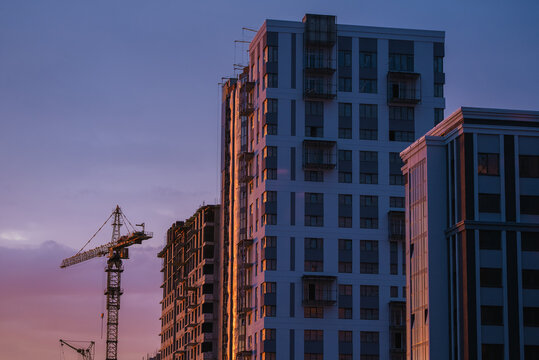 Tower cranes working on a construction site, building modern residential high-rise apartment buildings at sunset, creating a vibrant and dynamic urban landscape - Powered by Adobe