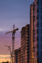 Tower cranes working on a new residential building construction project at sunset, showcasing urban...