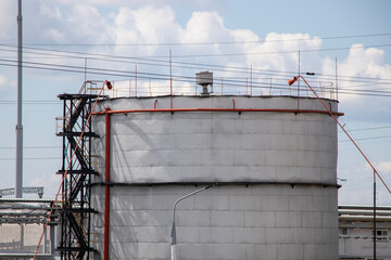 Tall industrial storage tank with piping against a blue sky in an urban setting