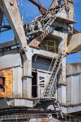 Rusty industrial crane against a clear blue sky at a port during mid-afternoon sun