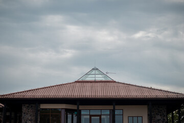 A contemporary house featuring a red-tiled roof and a central glass pyramid skylight under a...