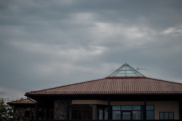A contemporary house featuring a red-tiled roof and a central glass pyramid skylight under a cloudy, overcast sky.