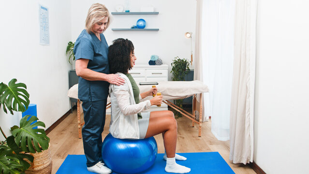 A Senior Physiotherapist Guides a Young Black Client Through Targeted Rehabilitation Exercises Using Stability Ball and Dumbbells