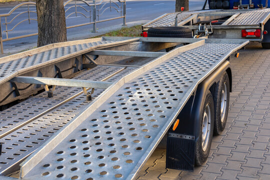 A flatbed trailer is parked along a city sidewalk with its metallic surface shining in the late afternoon light while street traffic moves nearby