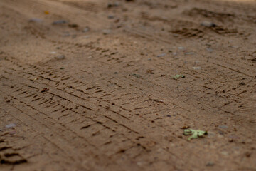 Faint tire tread marks with small pebbles scattered across sandy terrain, showing natural texture and vehicle movement patterns.