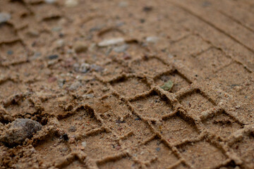 Detailed macro view of a vehicle tire tread imprint in sandy dirt, showing texture and geometric patterns left on the ground.