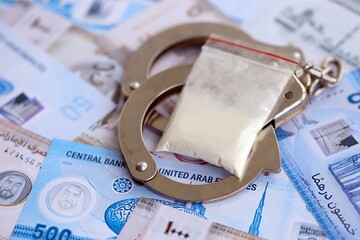 United Arab Emirates dirham currency money bills and cocaine pack with handcuffs. The concept of...