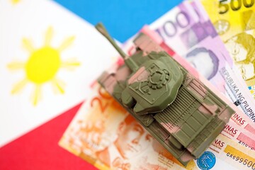 Philippines peso currency money bills and toy tank on flag. The concept of army funds and weapons...