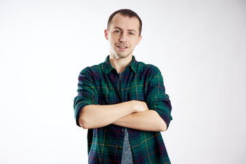 A man stands with arms crossed, wearing a checkered shirt and a casual gray top. He smiles...