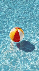 Obraz premium Colorful red, yellow, and white beach ball creates gentle ripples as it floats in the inviting, shimmering blue water of a resort swimming pool on a sunny day.