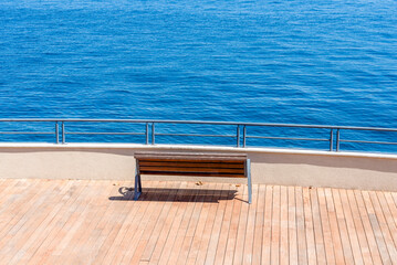 Peaceful wooden bench overlooking clear blue ocean on a sunny day at seaside promenade