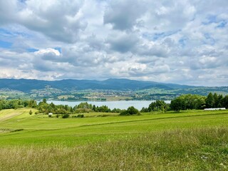 Panoramic summer view of Czorsztynskie lake with green fields and cloudy sky. Concept: eco tourism, scenic travel, outdoor exploration.	