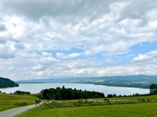 Panoramic summer view of Czorsztynskie lake with green fields and cloudy sky. Concept: eco tourism, scenic travel, outdoor exploration.	