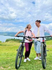 Obraz premium Happy smiling couple with bicycles on a cycling path near Czorsztyn and Czorsztynskie Lake with Tatra Mountains in the background, Poland. Concept of active lifestyle, love, adventure, and eco tourism