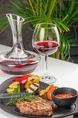 Grilled steak with vegetables, sauce, and red wine served on a black plate