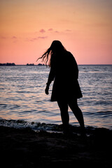 Vertical photo of a silhouette of a girl during sunset on the beach with the sea in the background