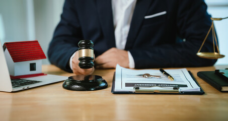 An Asian businessman in a suit holds a house model with a gavel, symbolizing real estate law, property auction, finance, and justice.