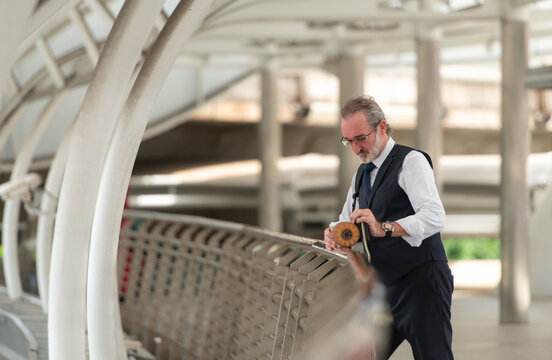 Smiling senior businessman holding a coffee cup and electric skateboard