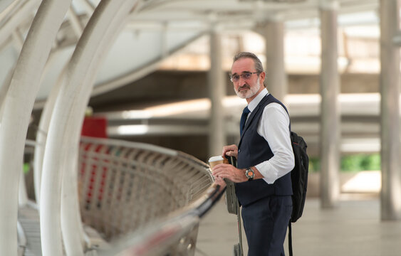 Smiling senior businessman holding a coffee cup and electric skateboard