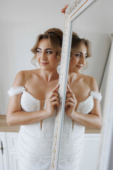Elegant bride admiring reflection in mirror before wedding ceremony in bright room
