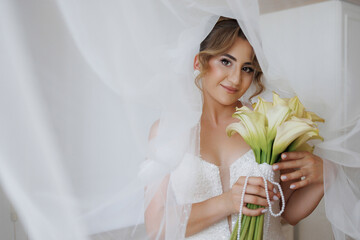 Bride holding calla lilies while draped in a delicate veil before the wedding ceremony
