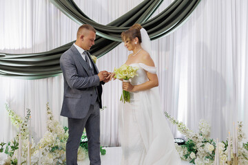 Couple exchanges wedding vows in elegant indoor venue adorned with floral decorations