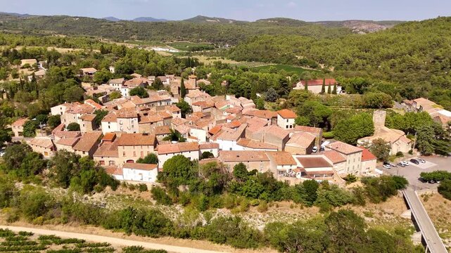 Aerial view of the village of Agel, France, nested in the hills of Occitanie, with traditional terracotta colored houses and a castle, surrounded by vineyards and forests.