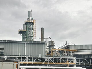  a wide shot of an industrial factory or refinery against a cloudy sky. The complex is full of intricate piping, smokestacks, and ladders, emphasizing its scale and the heavy industrial nature of the 